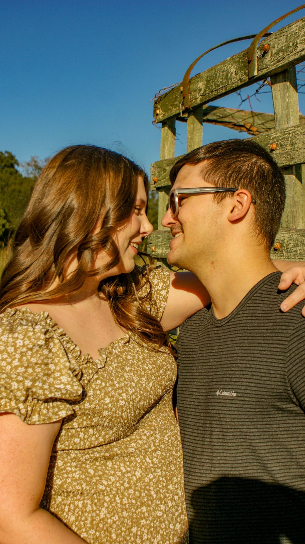 An intimate maternity portrait against a rustic wooden structure in warm sunlight.
