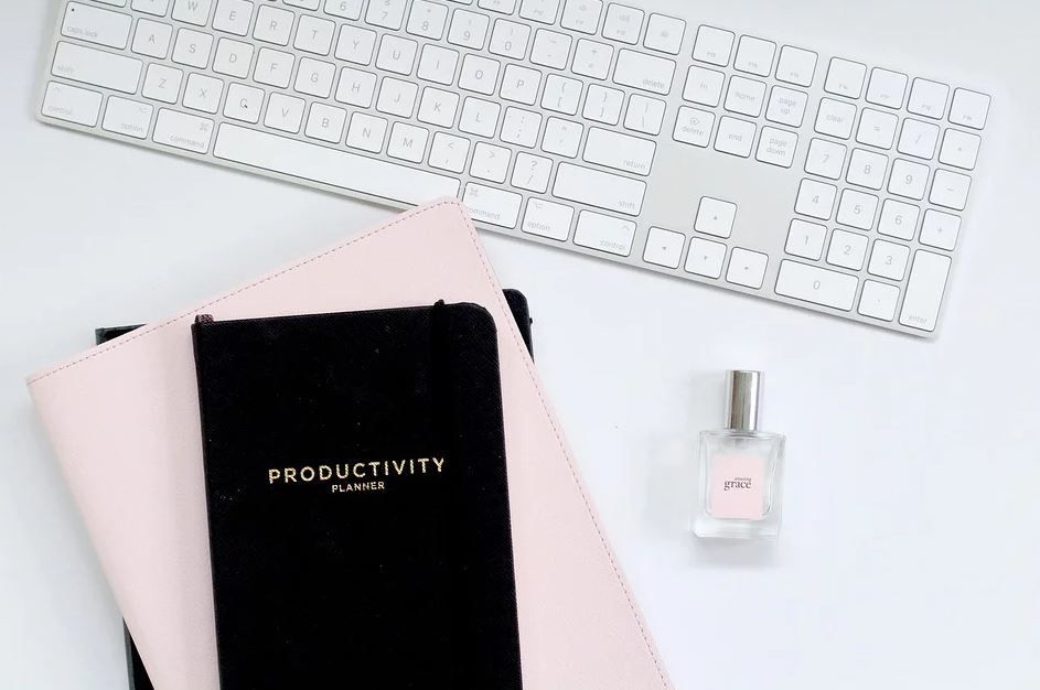 Minimalist desk arrangement with white keyboard, black productivity planner, and pink accents.