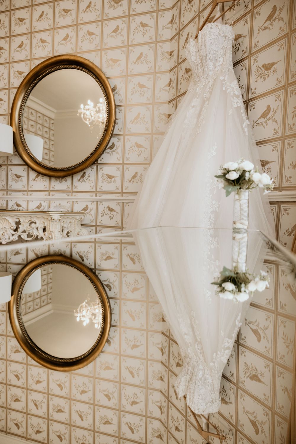 Wedding gown reflection in round gold mirrors against vintage wallpaper with floral accents.