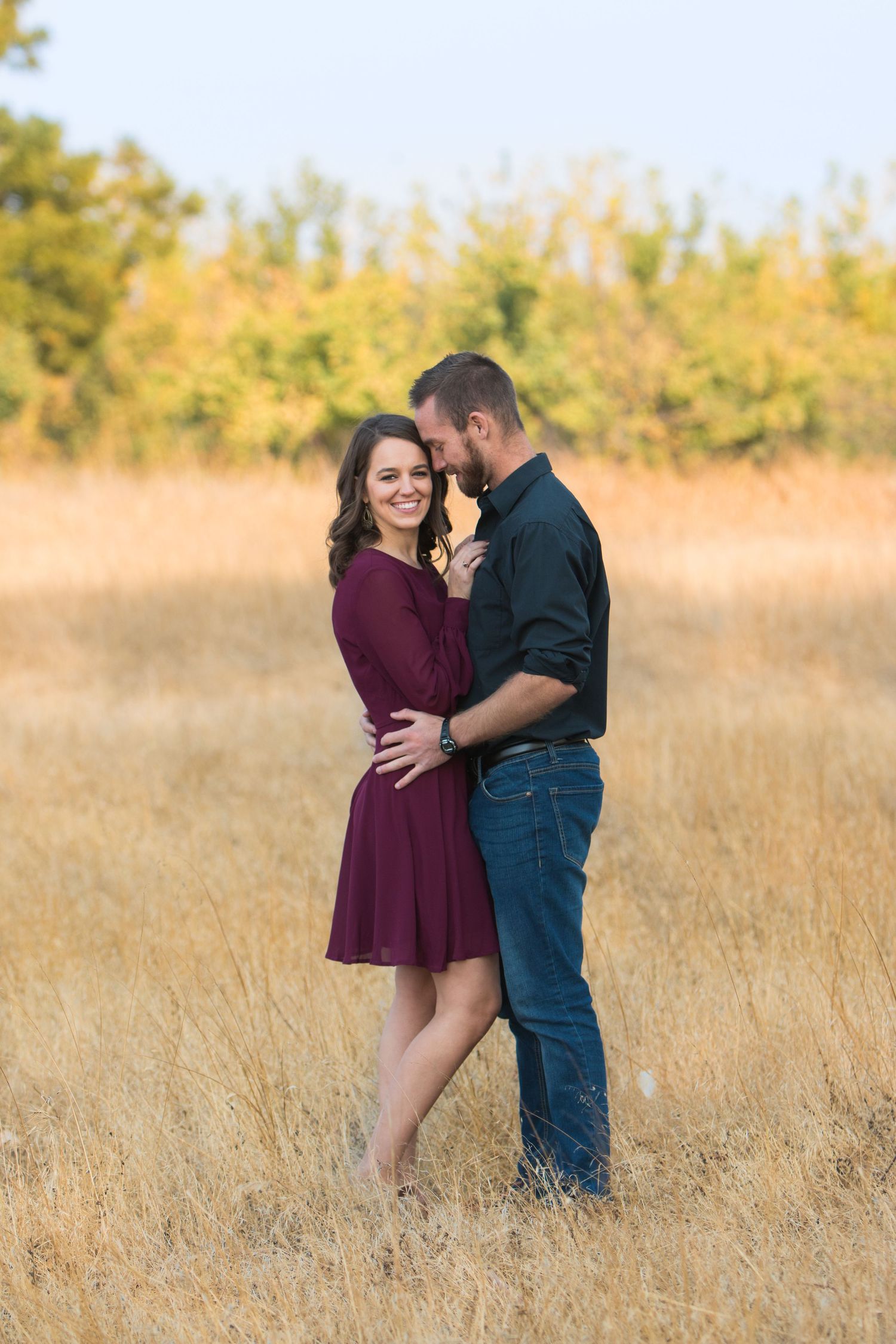 Engaged couple in field of golden grass with orchard in background. Orland, California