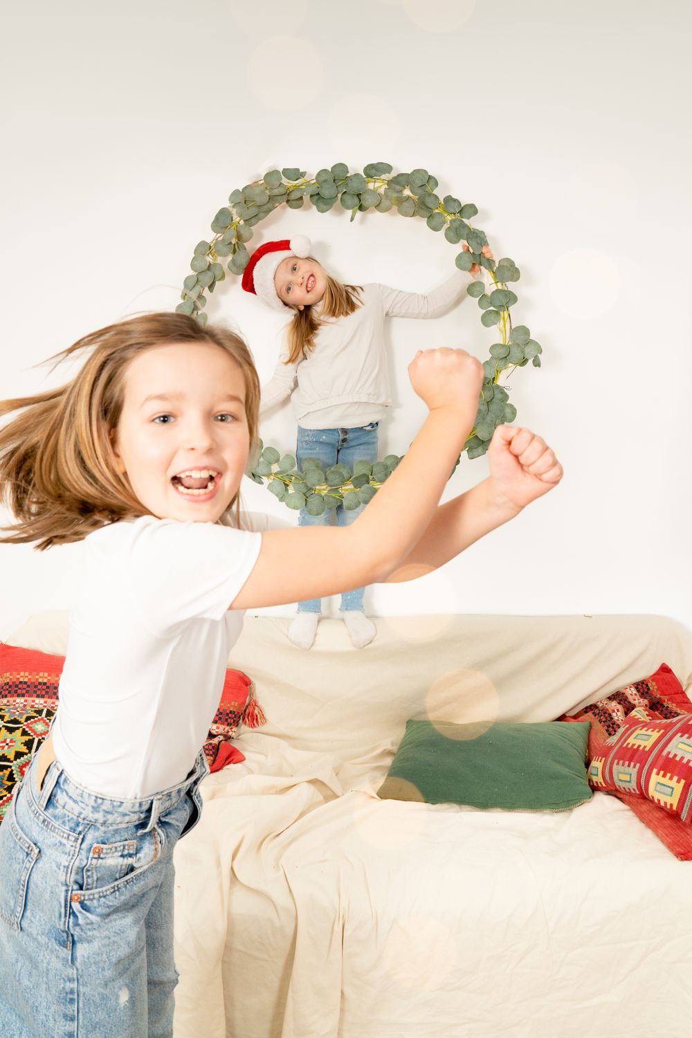 People playing and jumping with joyful energy near a decorative wreath and festive holiday decor.