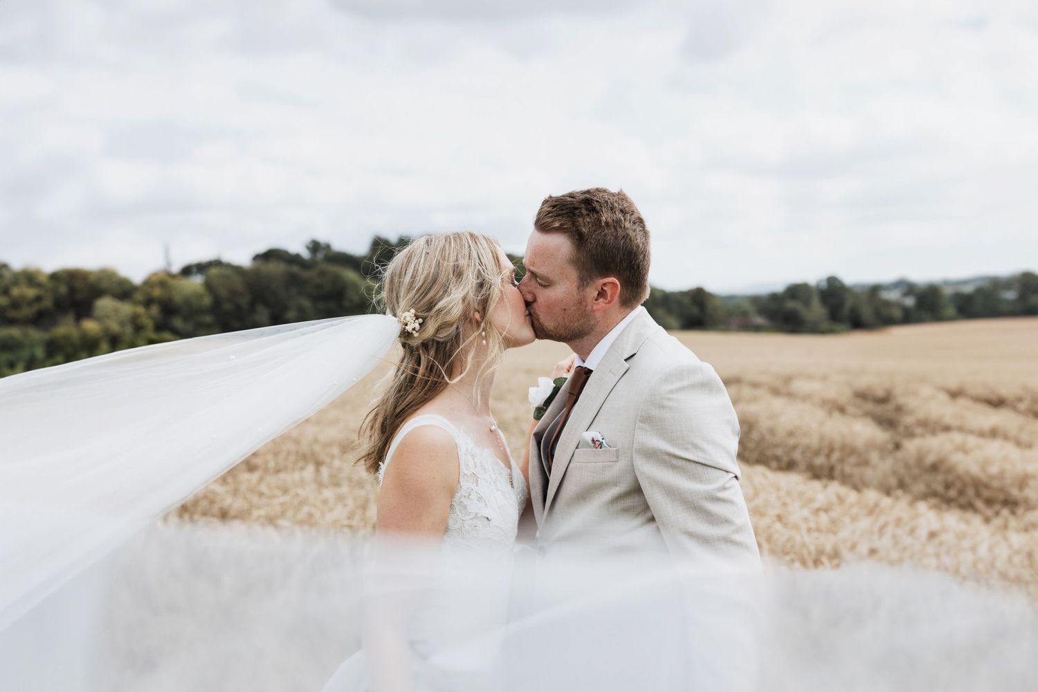 Abbie and Rob kissing in a field in their wedding attire in Sussex