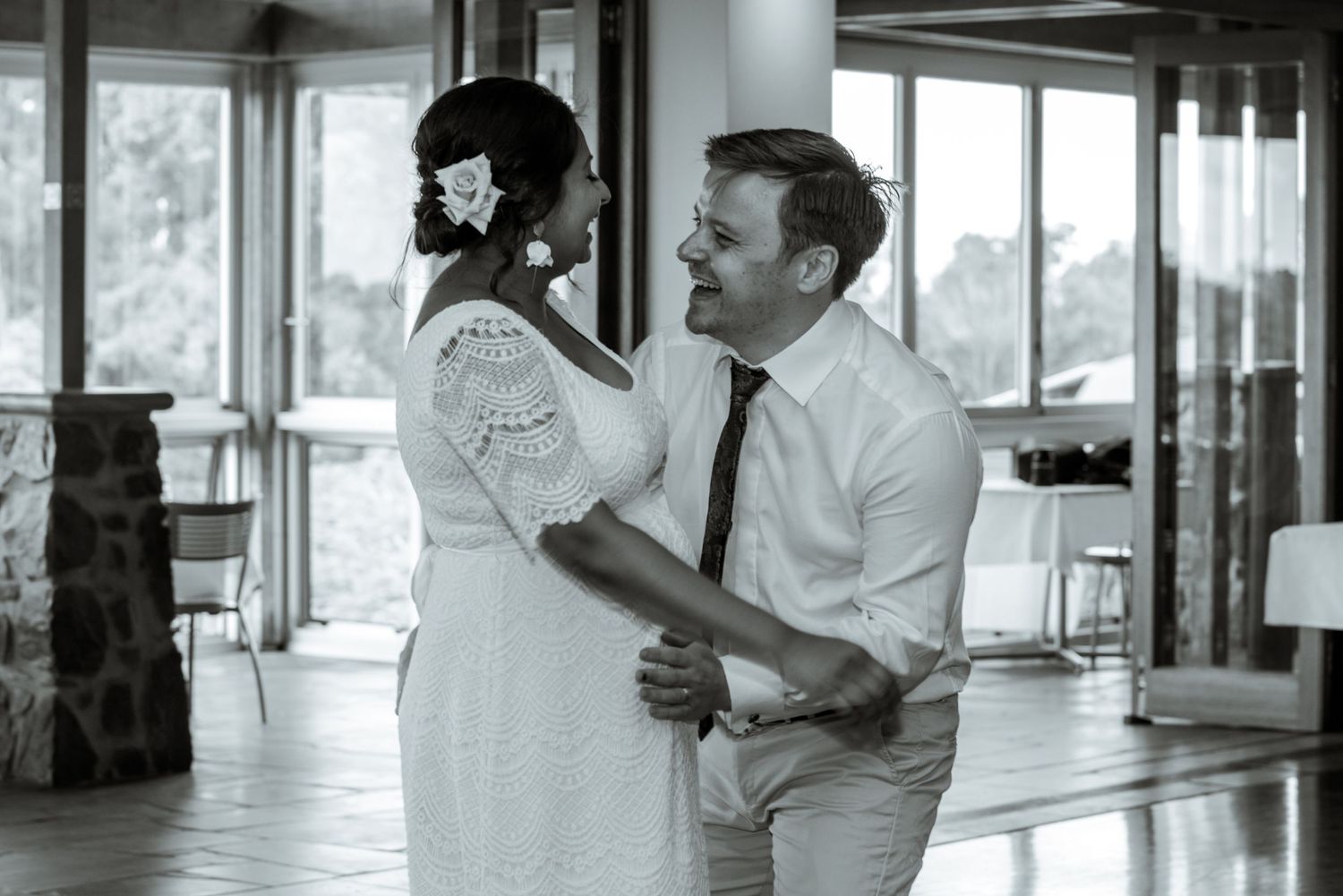 Black and white photo capturing intimate dance moment in spacious venue with windows.