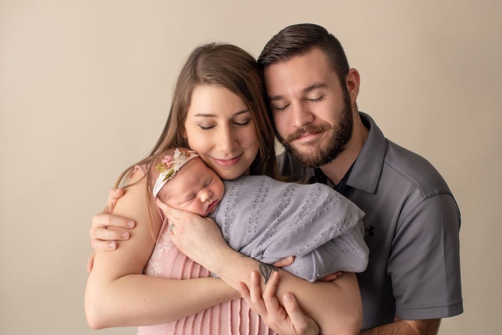Intimate family portrait session with newborn in soft neutral colors against beige background.