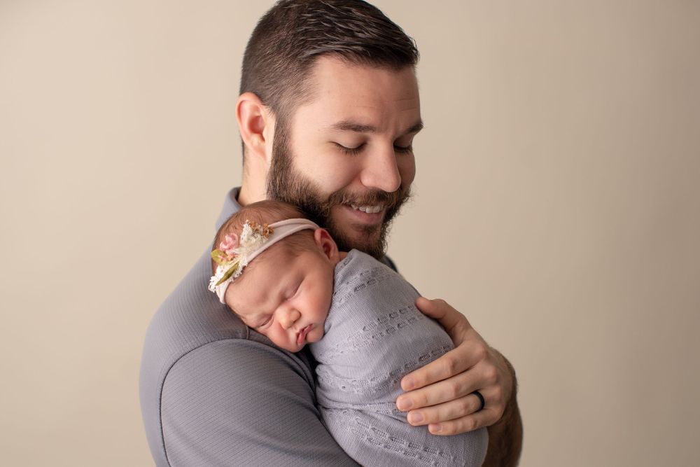 Sweet portrait capturing tender moment with sleeping newborn in grey onesie.