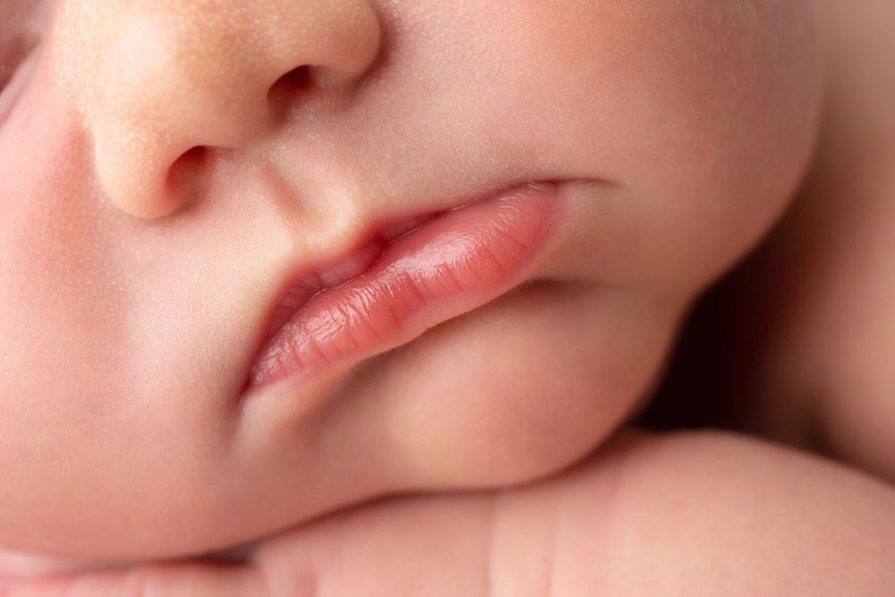 Macro photograph showing delicate pink lips and nose of sleeping newborn.