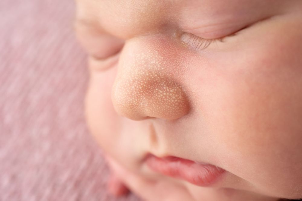 Extreme close-up macro photo of newborn baby's nose and lips against pink background.
