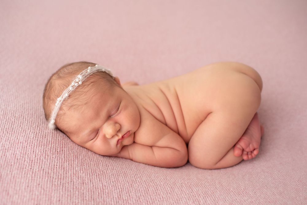 Newborn baby sleeping peacefully on pink textile wearing white lace headband.