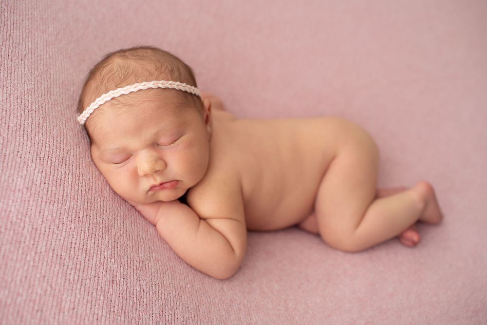 Peaceful sleeping newborn posed on pink background wearing dainty headband.
