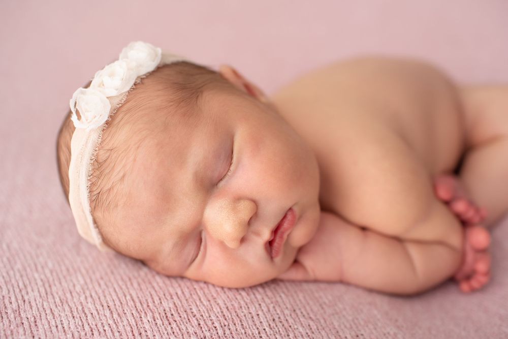 Sleeping newborn with floral headband photographed on pink fabric.