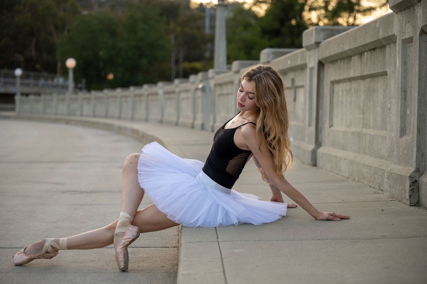 Dancer in black and white costume stretches elegantly along concrete path with stone railings.