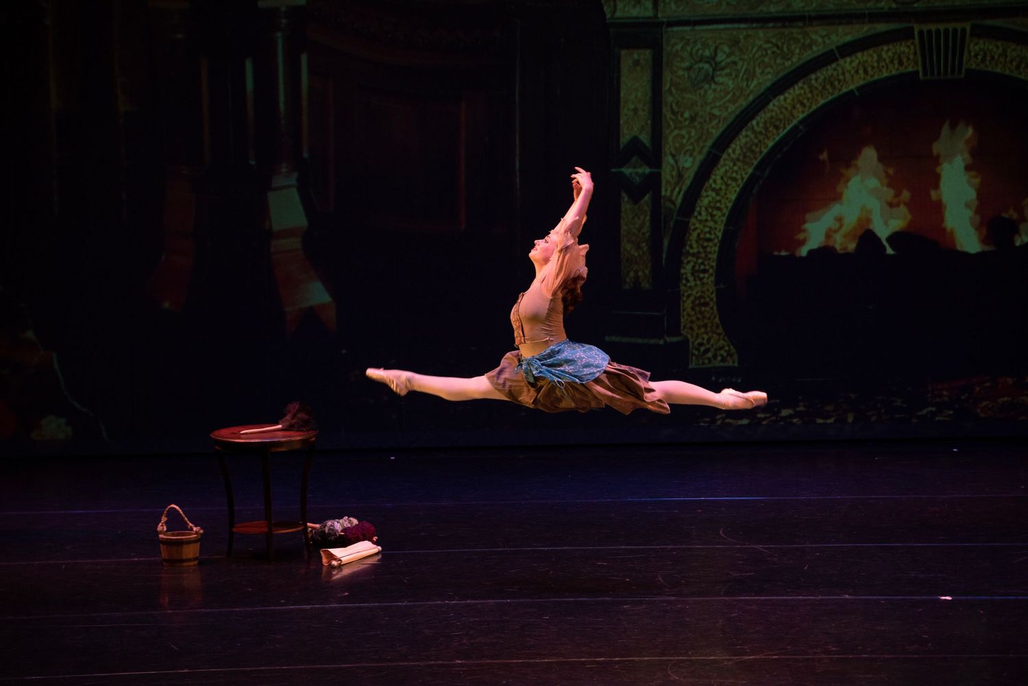 Dancer performing dramatic split leap on dark stage during performance.