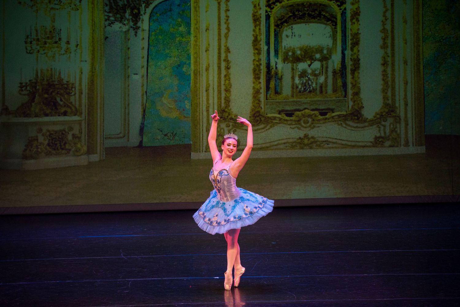 Ballerina performing en pointe in purple tutu on stage with ornate backdrop.