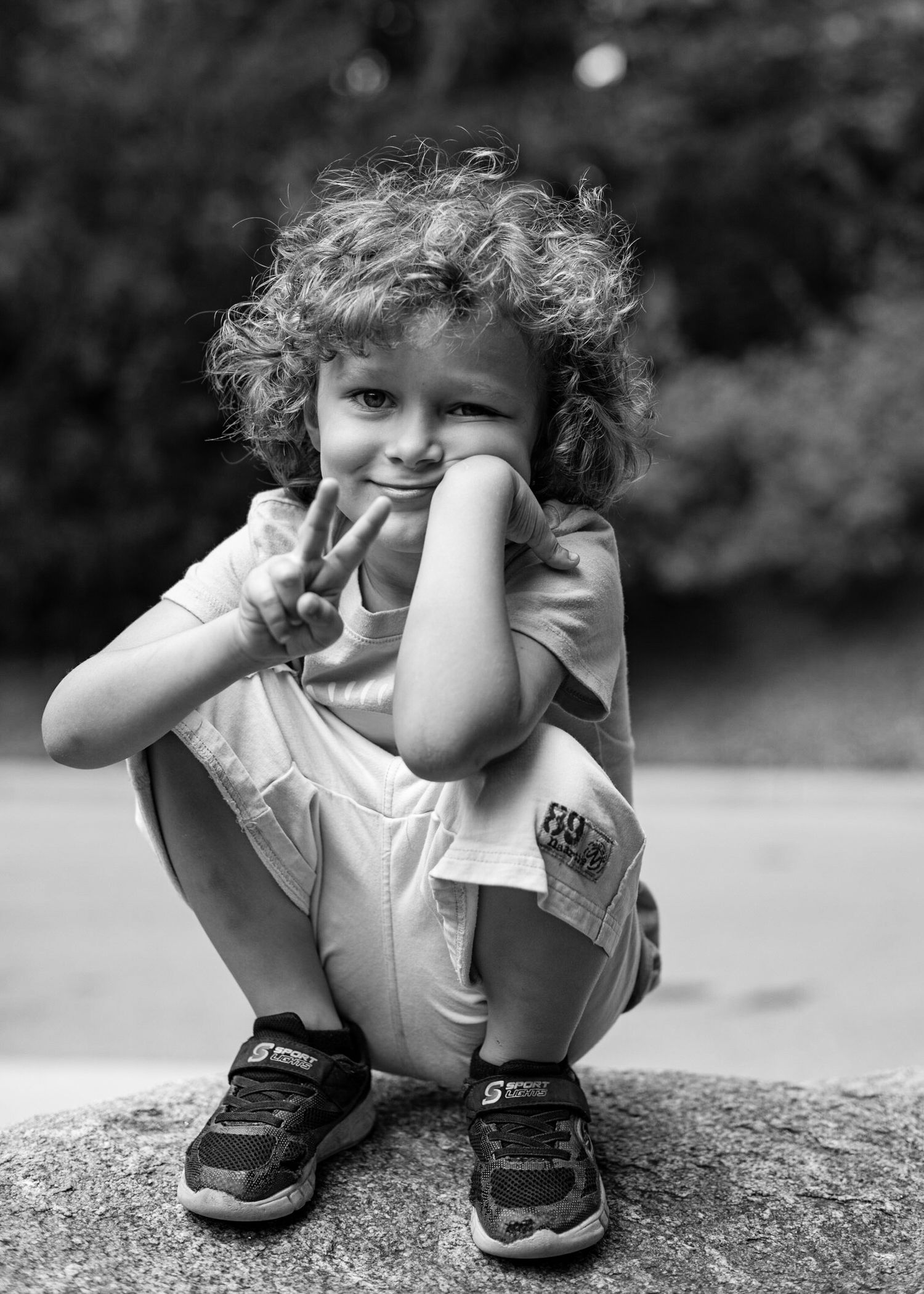 Black and white portrait of young child crouching outdoors.
