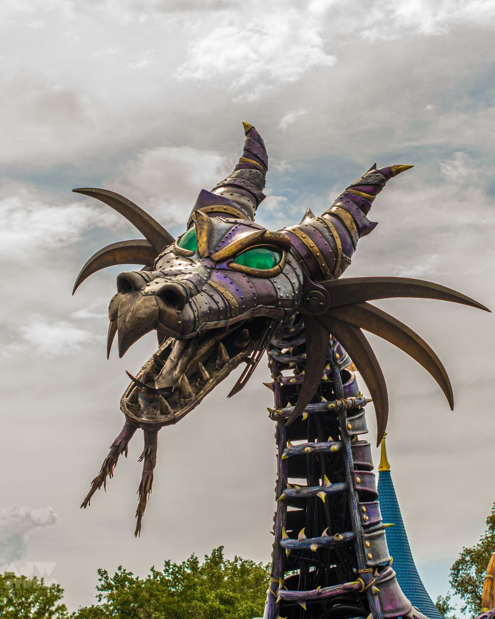Metallic dragon head sculpture with glowing green eyes displayed at theme park.