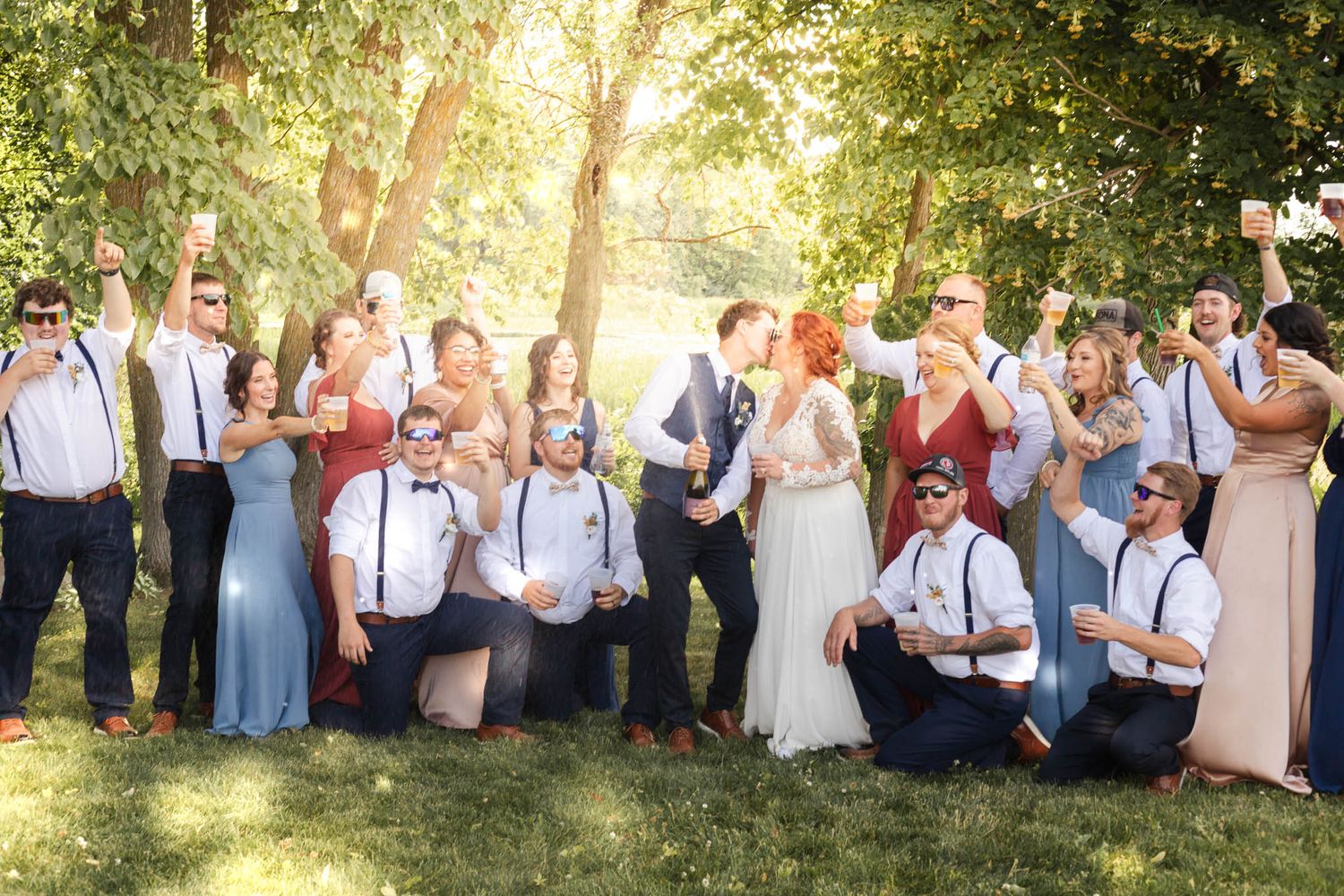 A groom popping champagne while kissing his bride with the bridal party raising a glass at Pondview Farm in Central, MN