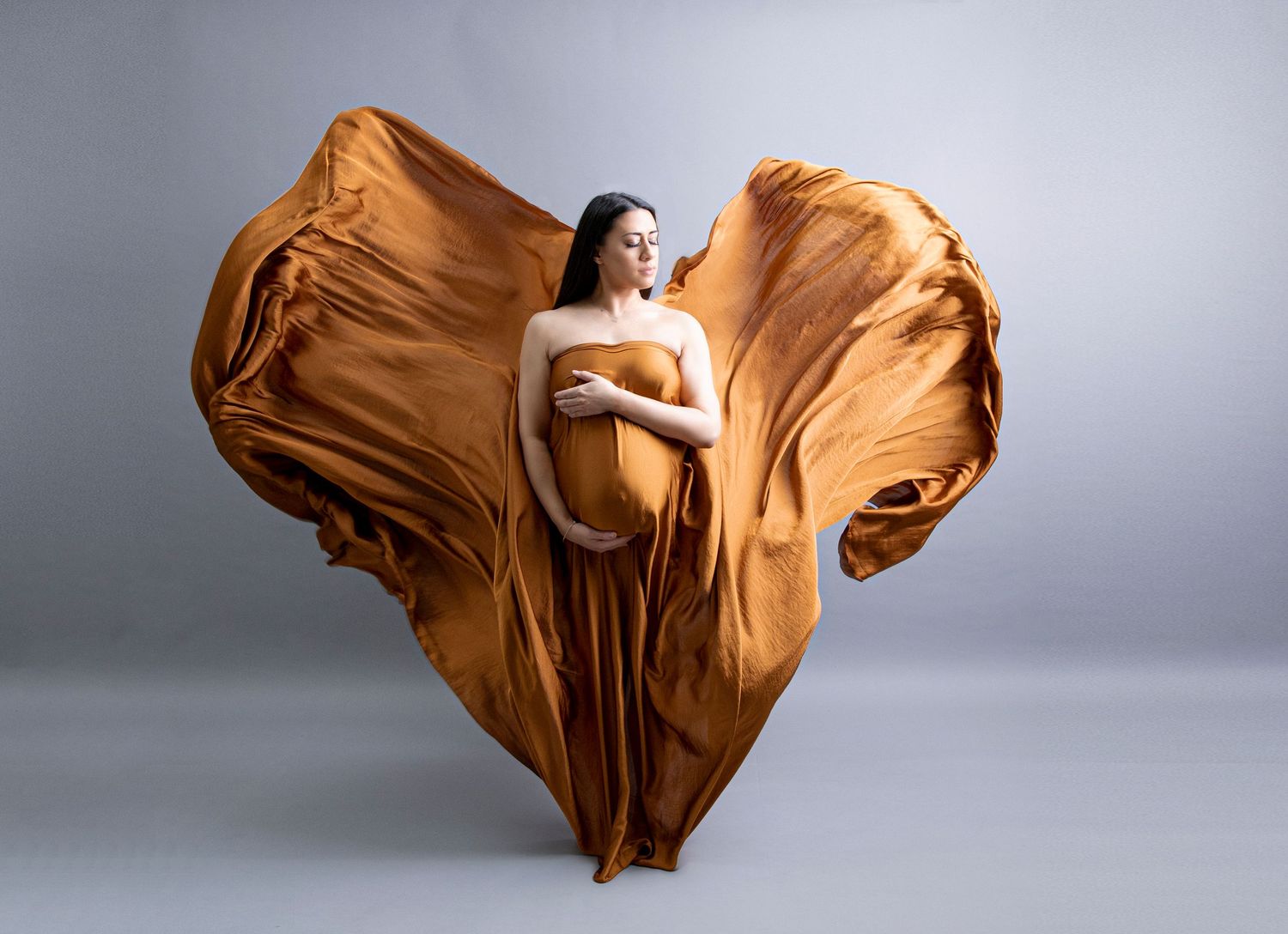 Fine Art Maternity Shoot, Brunette mum to be draped in Cognac,Copper,Burnt Orange Silk material, against grey backdrop