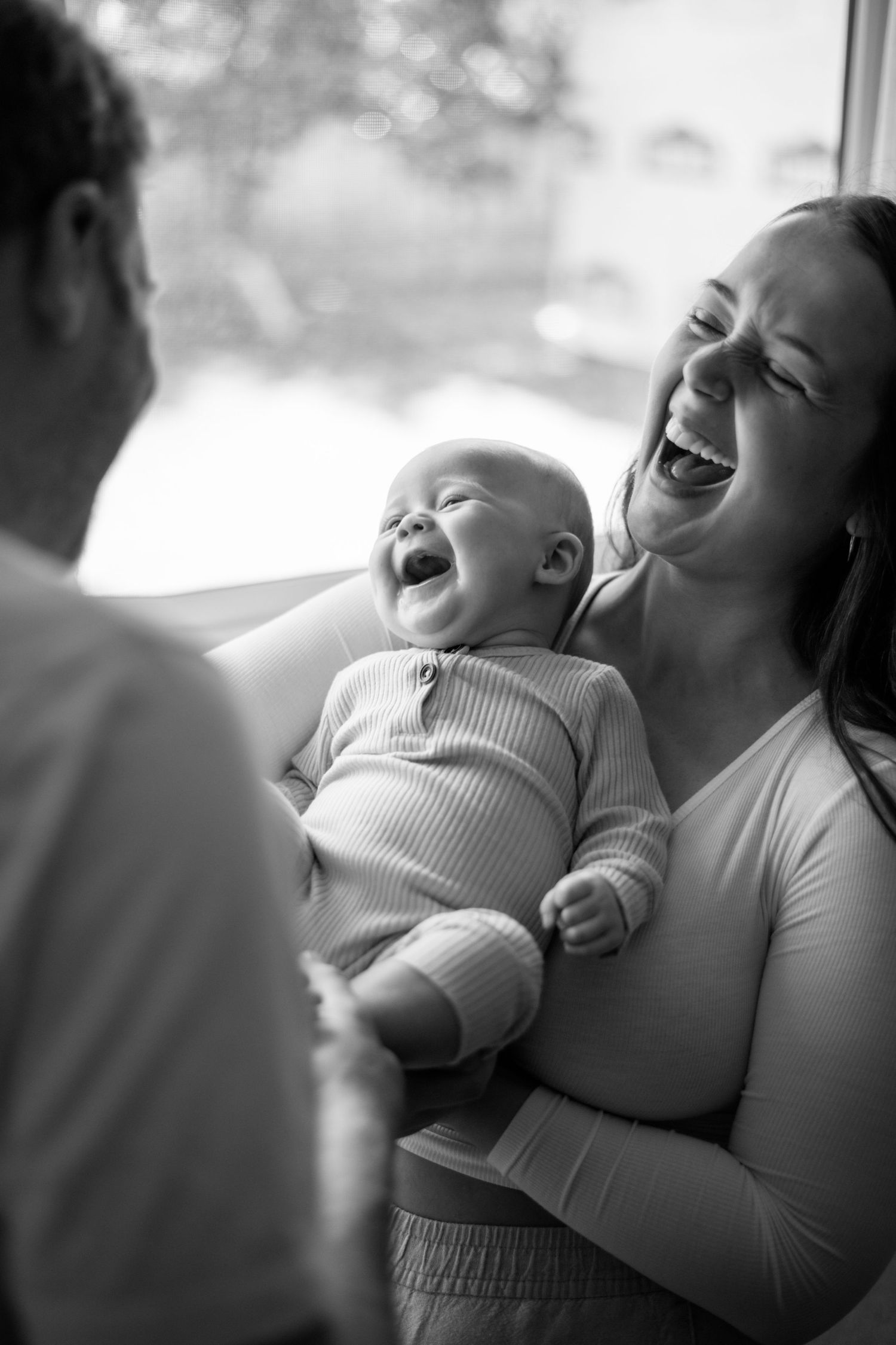 A joyful black and white candid photo captures shared laughter between a baby and parent.