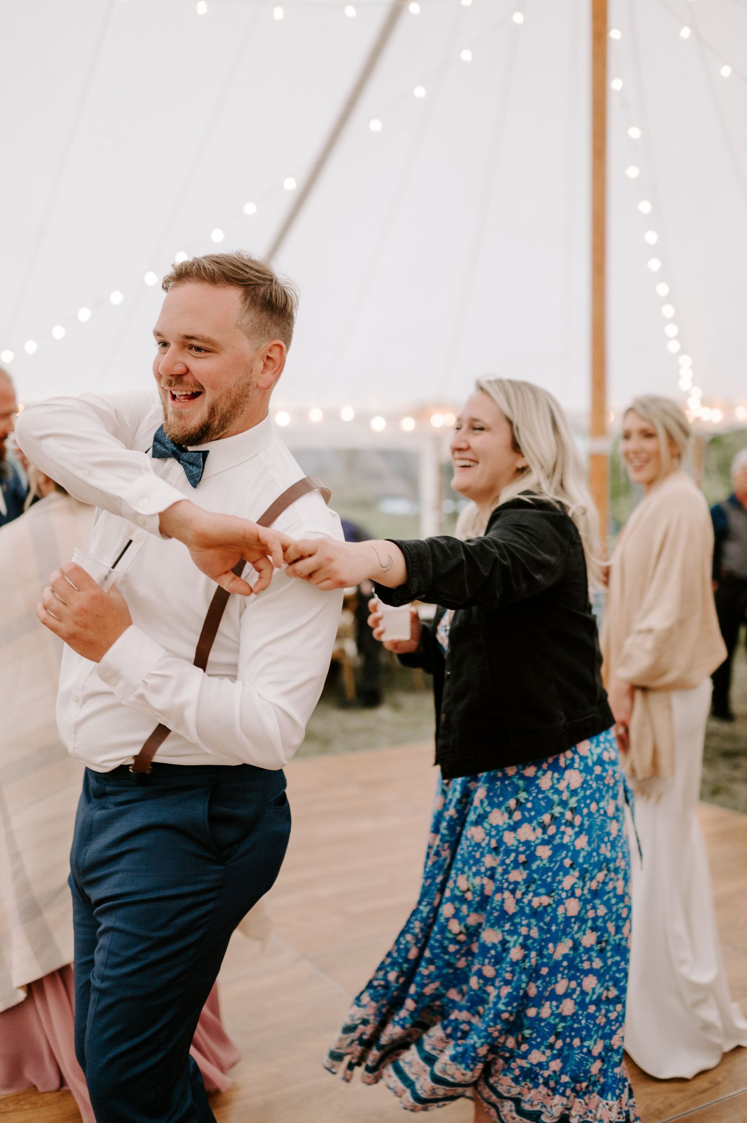 Couples dancing energetically at a wedding reception under string lights.