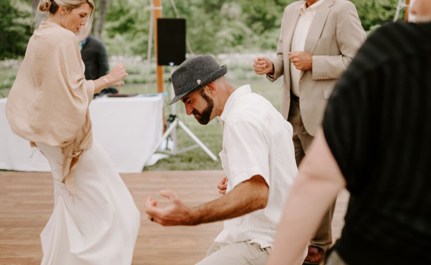 Guests dancing together at a wedding reception under a white tent with string lights.