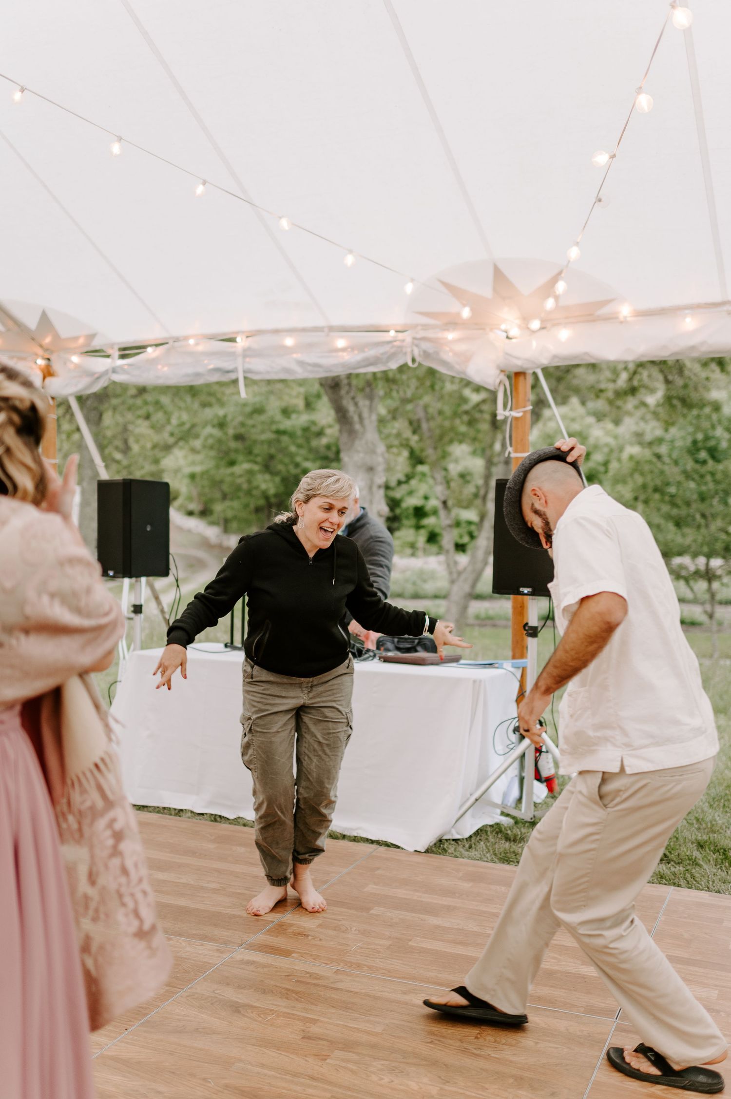 Guests showing off energetic dance moves on wooden floor under tent at wedding reception.