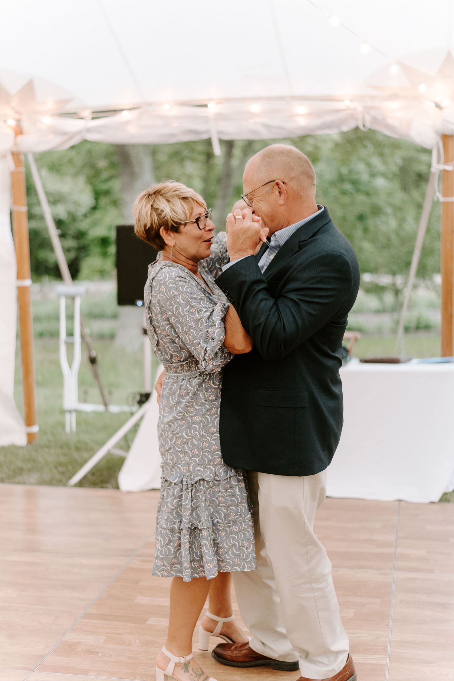 Couple sharing a playful dance moment under string lights at wedding reception.