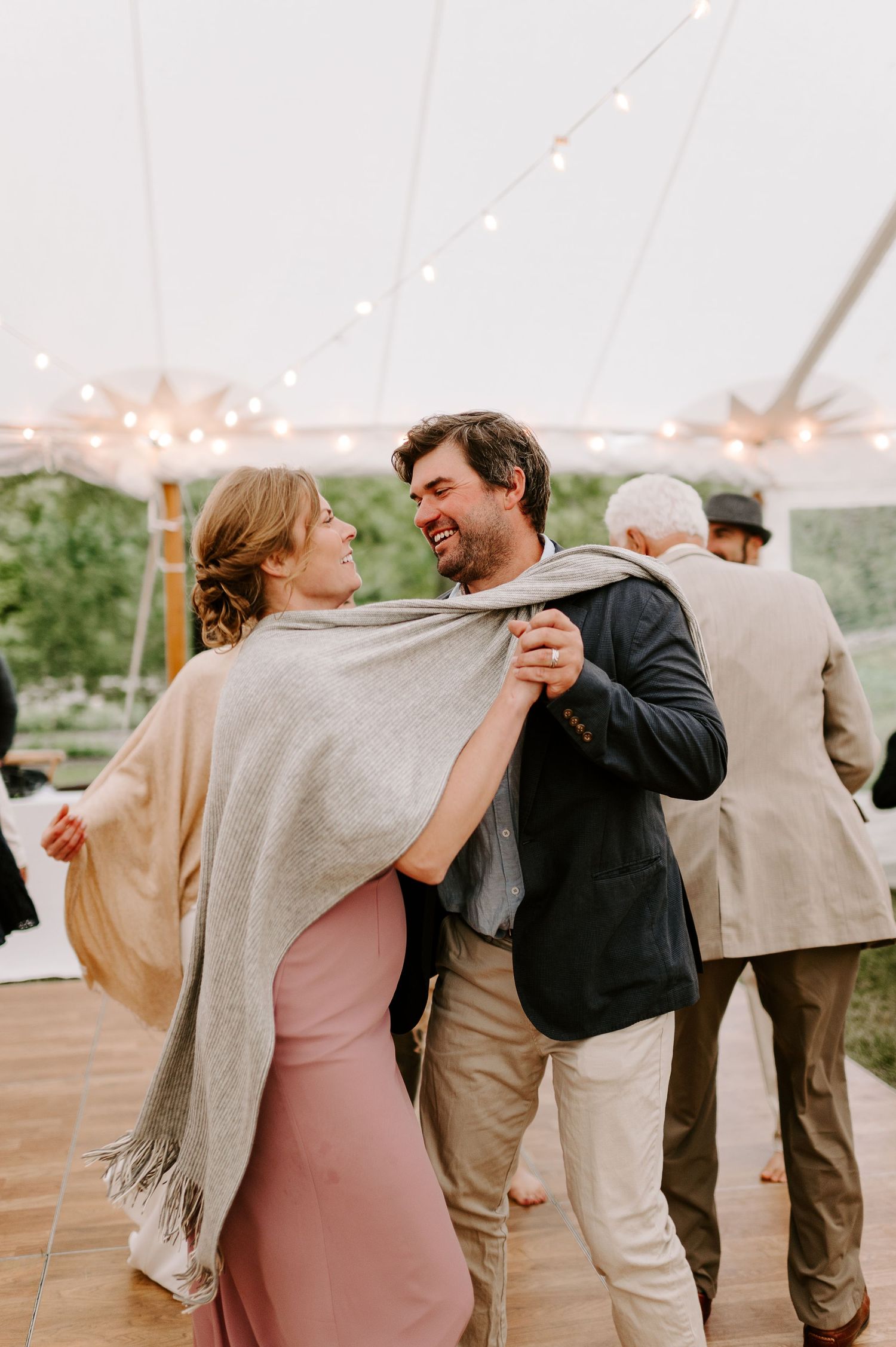 Dancing couple wrapped in a cozy gray shawl at an outdoor wedding reception.