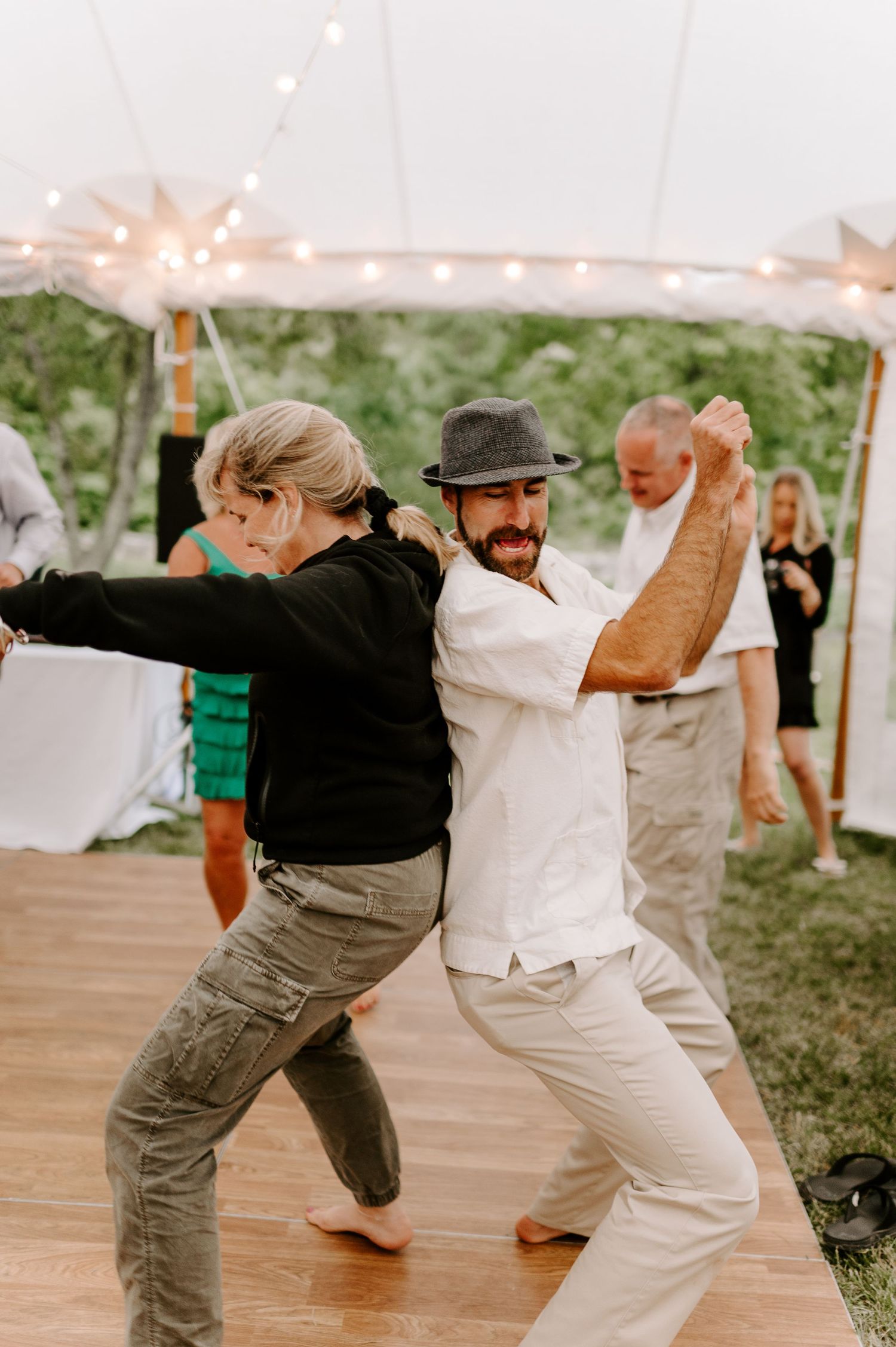 Dancers perform a synchronized line dance routine on a wooden dance floor under a tent.
