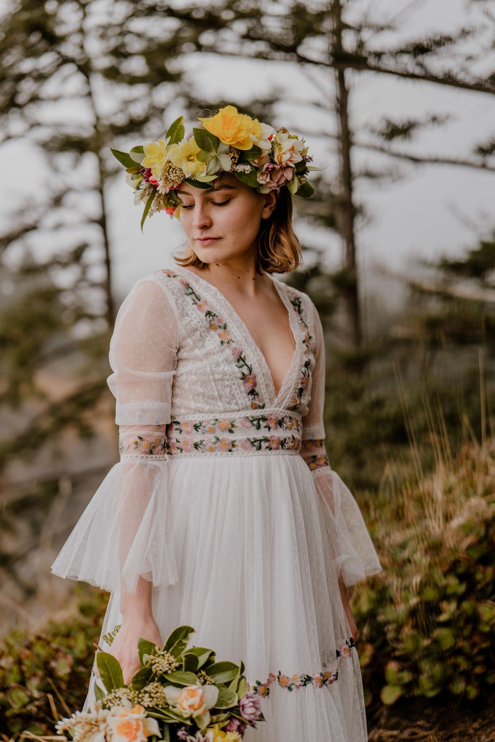 Bride with floral head dress and boquet in a tree clearing looking to her right