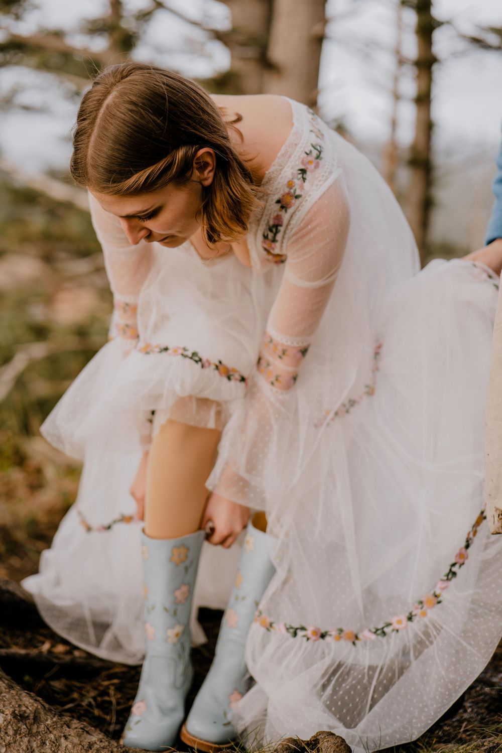 Bride in white dress putting on blue floral cowboy boots