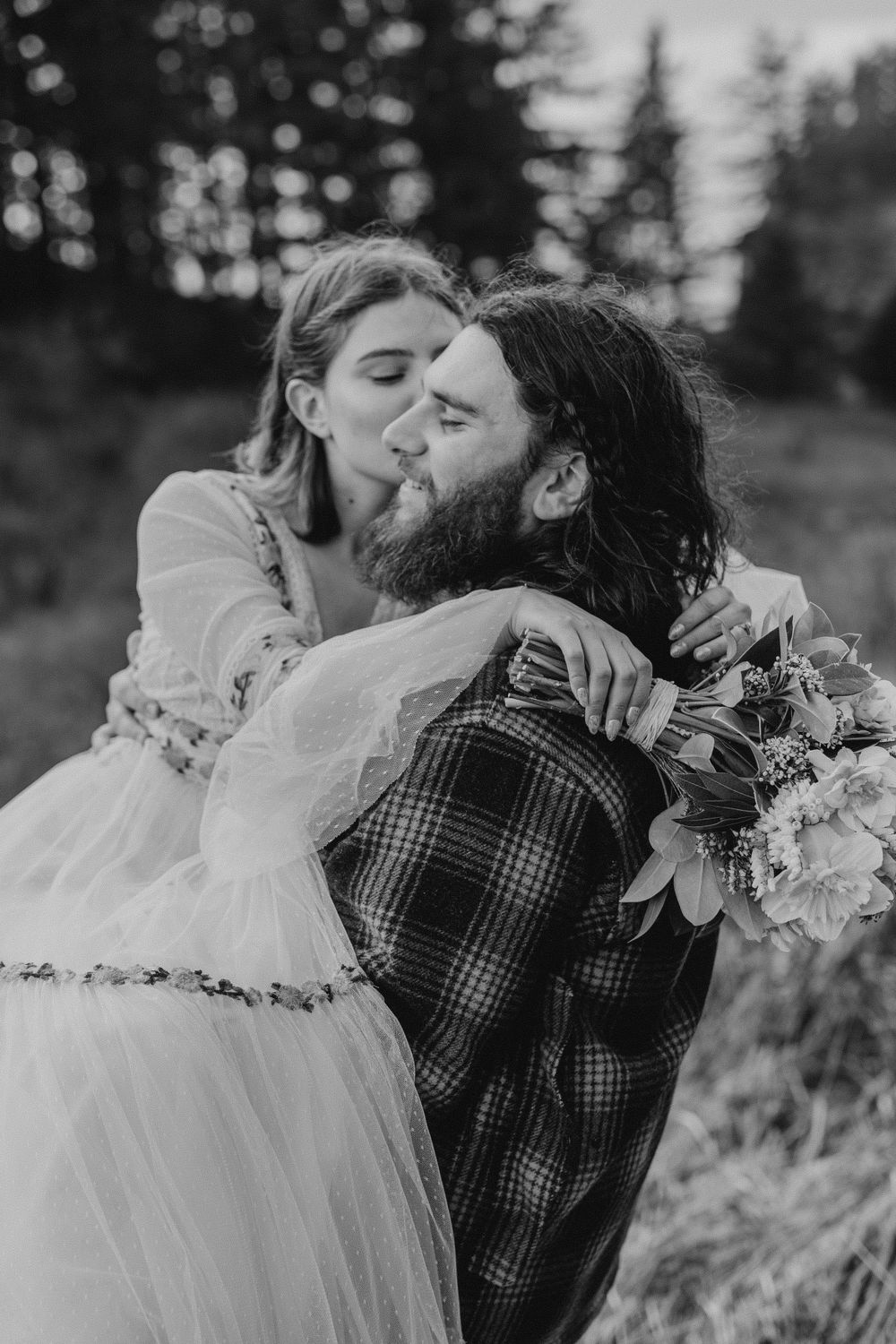Groom carrying bride while bride kisses him on the cheek