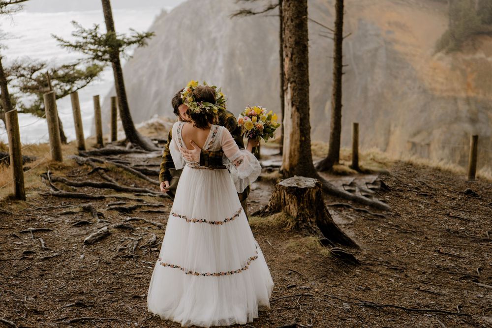 Groom hugging bride after first look on cliff overlooking Oregon ocean