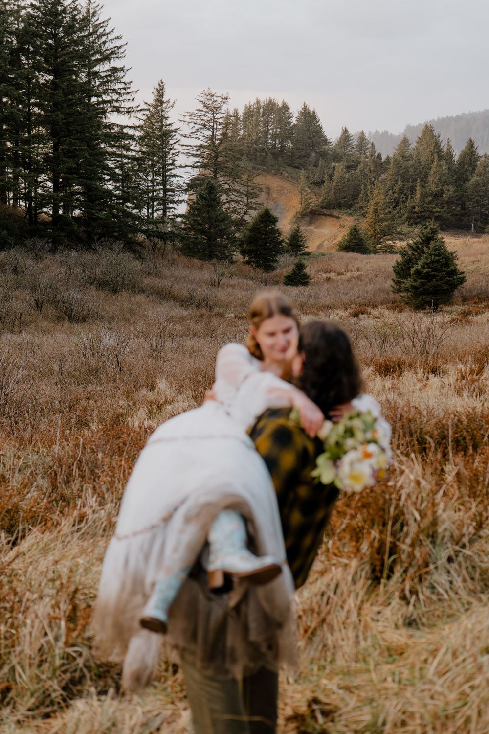 Blurry photo of Groom carrying bride in grassy field while bride looks at him