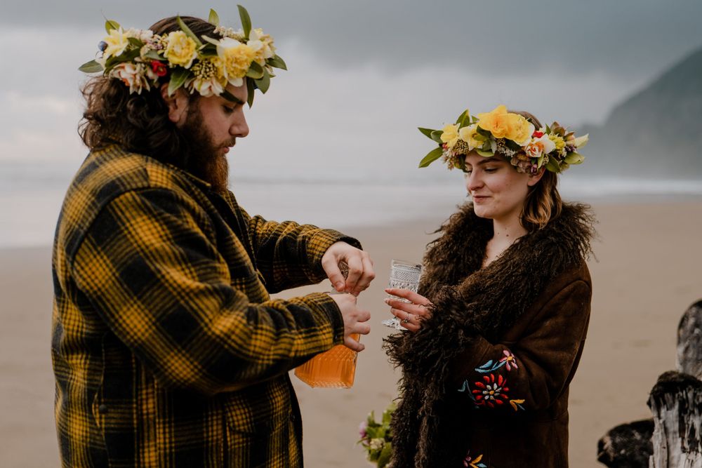 Groom opening a glass bottle with bride next to him on the oregon beach