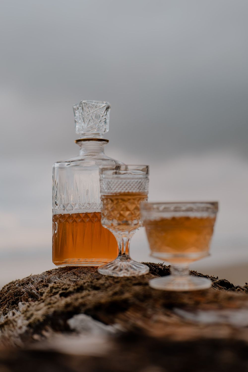 Class cups and bottle filled with orange liquid sitting on a rock at the oregon coast