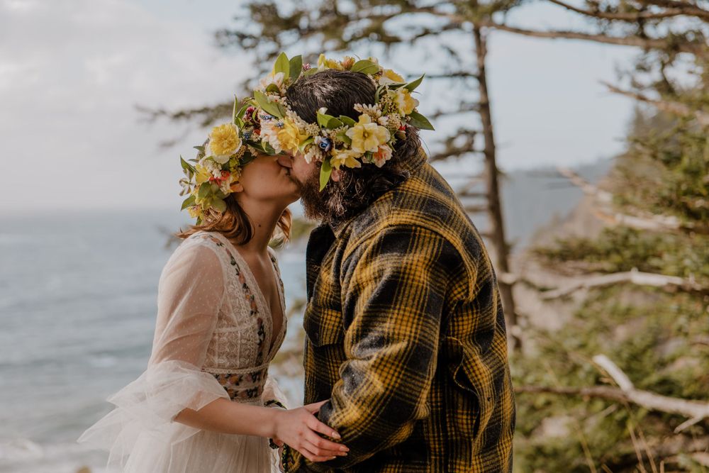 Bride and groom first kiss alongside cliff overlooking Oregon coast
