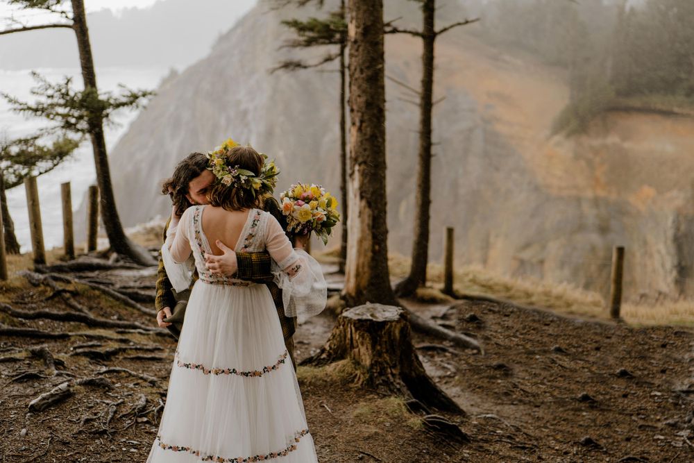 Groom hugging bride after first look on cliff overlooking Oregon ocean