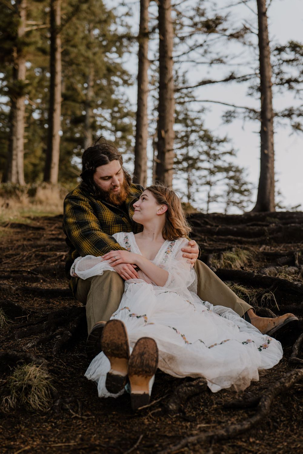 Bride sitting on grooms lap on forest path and looking at groom