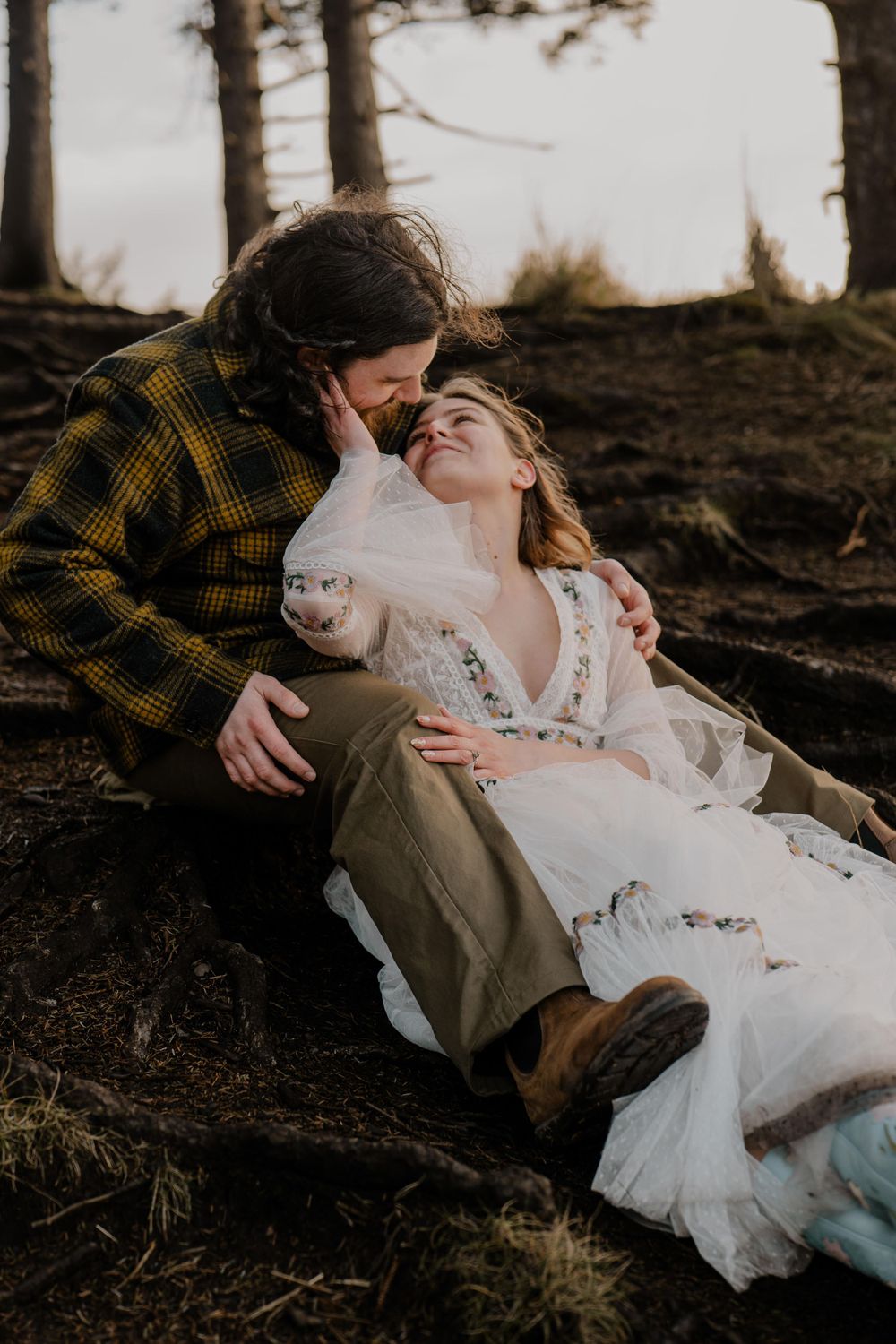 Bride resting hand on grooms cheek while sitting on his lap and looking at him