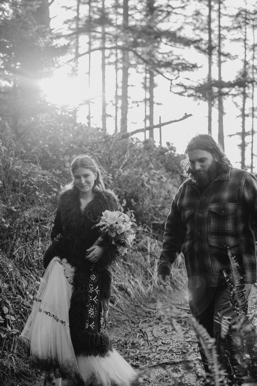 Black and white of groom leading bride down a forest past after ceremony