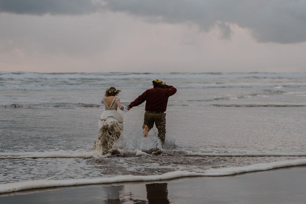 Bride and groom running through ocean tide into the waves