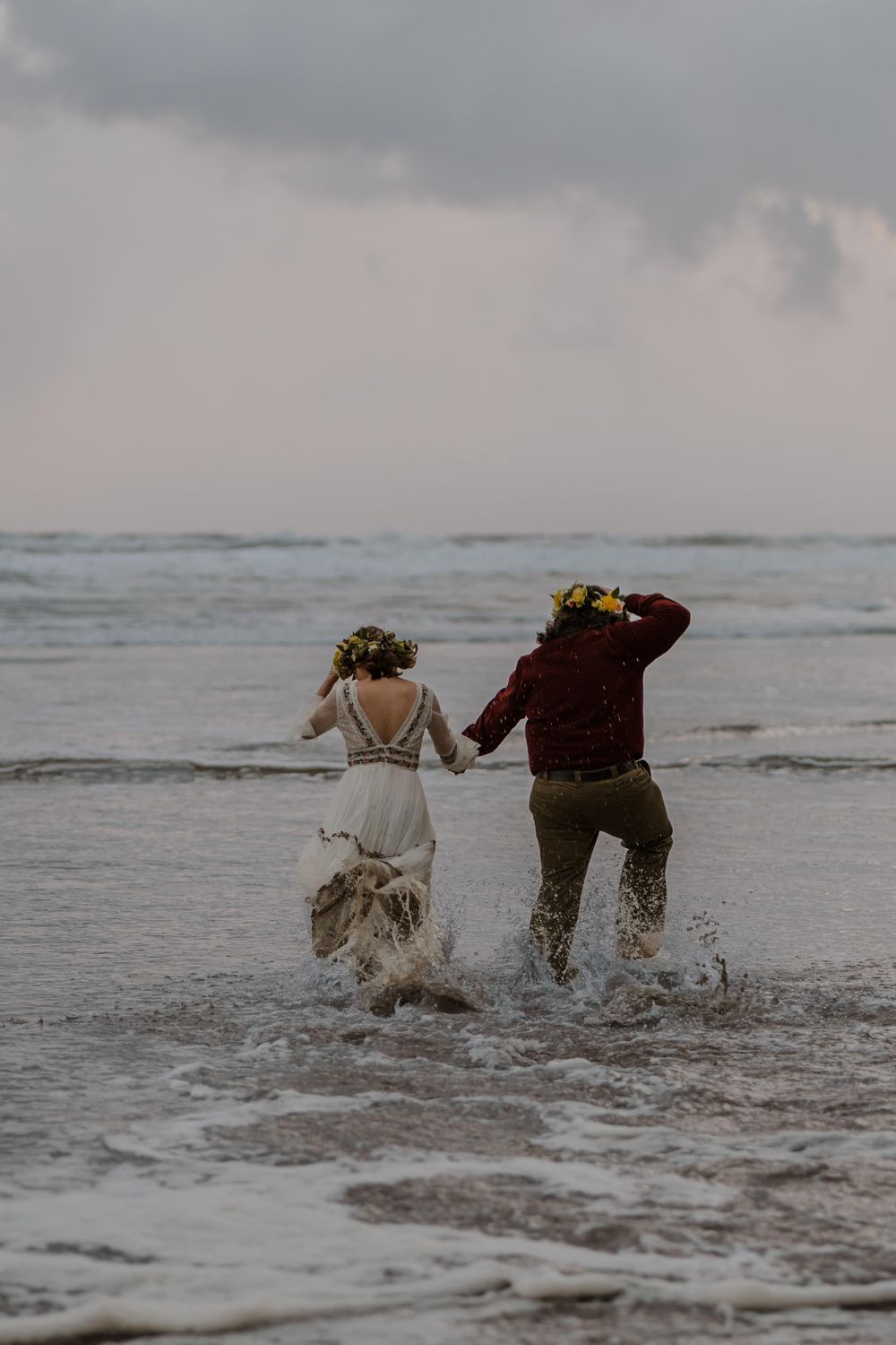 Bride and groom running through ocean tide into the waves