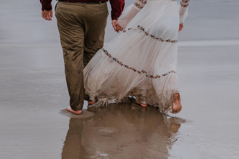 Bride and grooms lower half walking on beach with wet and sandy clothes