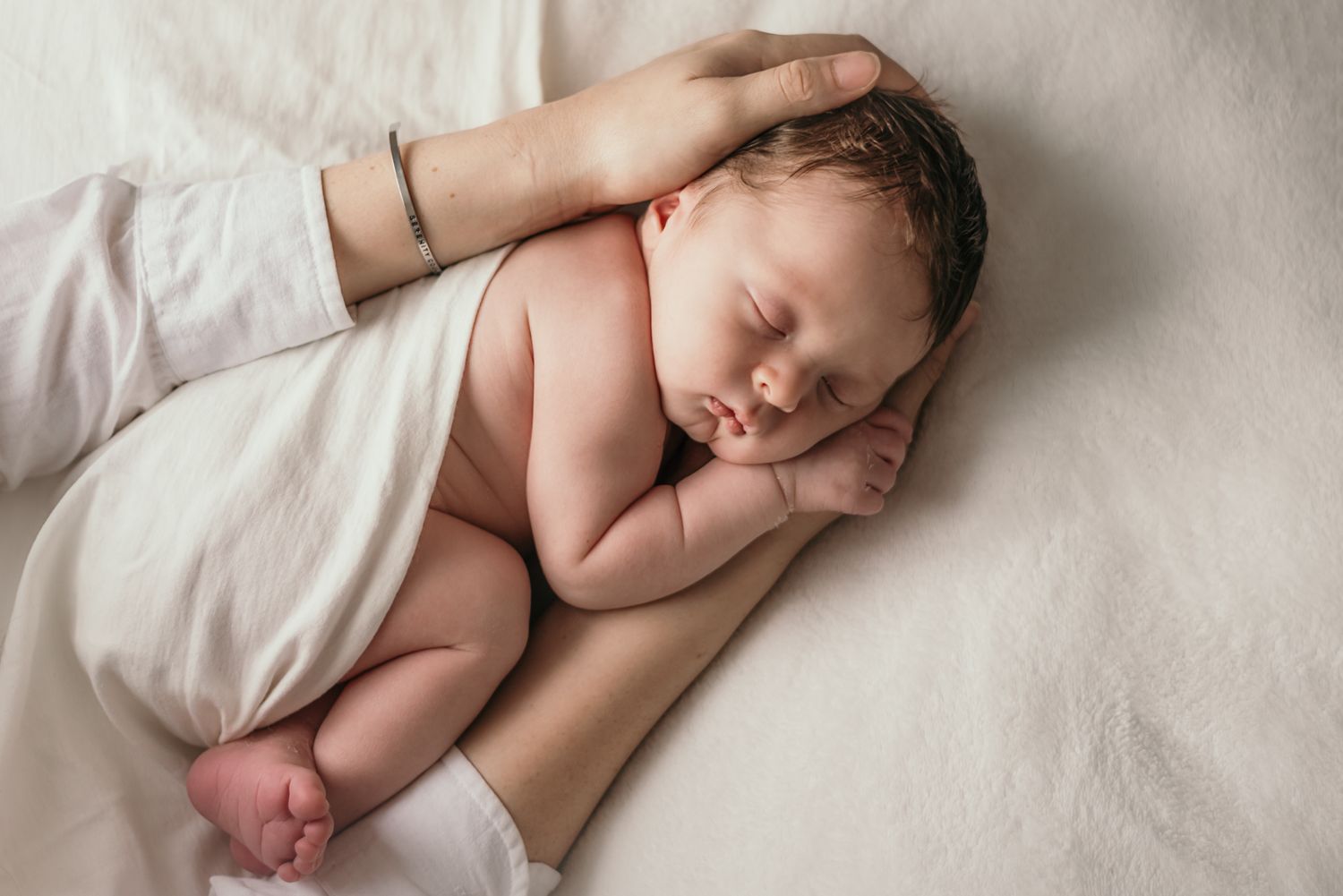 Gentle touch comforts sleeping newborn on white bedding.
