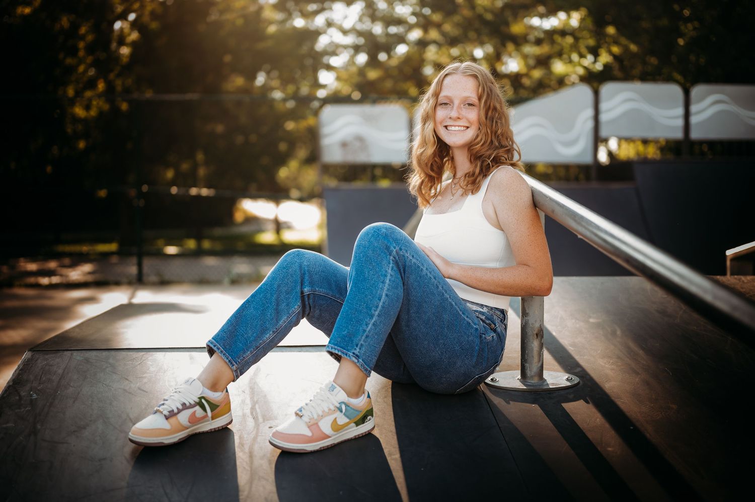 Smiling teenage girl sitting on skate ramp during golden hour senior portrait.