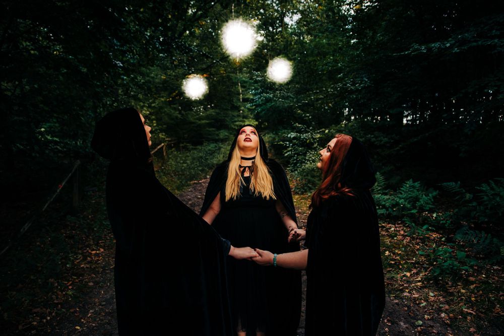 Mystical glowing orbs float above three cloaked figures in a dark forest.
