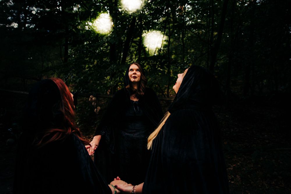 Ethereal light orbs illuminate a group gathered in dark robes within a forest.