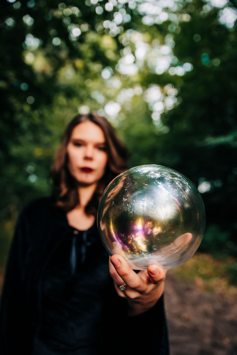 A crystal ball held up against a blurred forest background reflects light in an ethereal way.