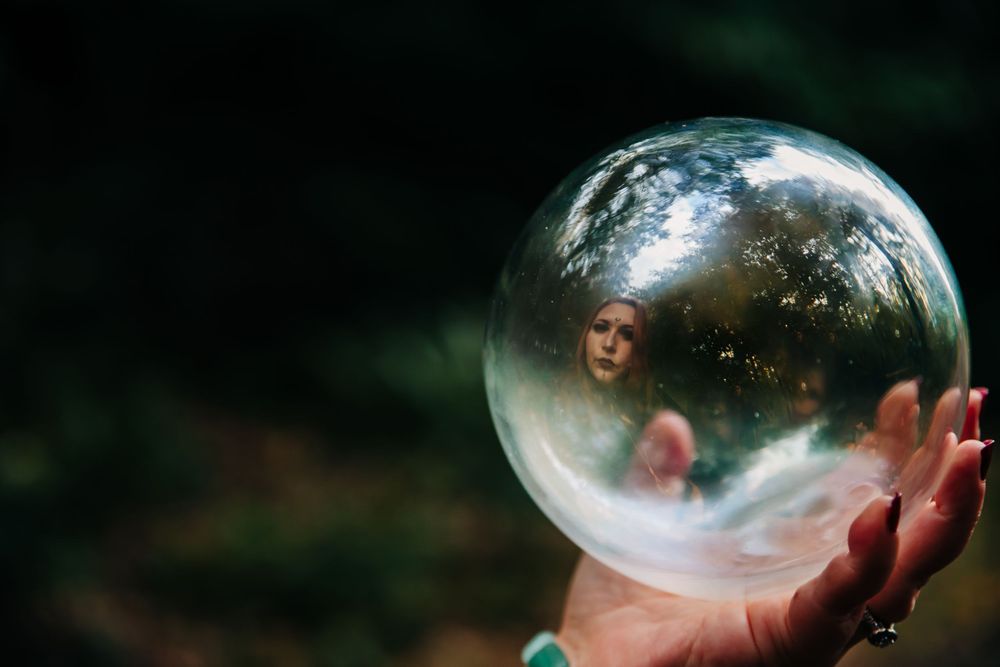 Clear glass sphere being held up to capture reflections in a magical outdoor setting.