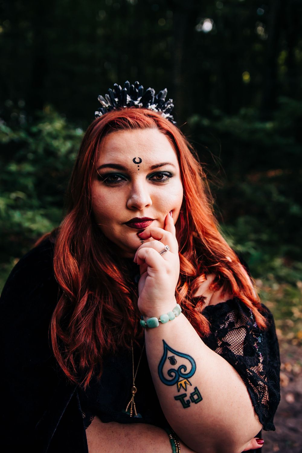 Gothic styled portrait with dark crown and lace in forest setting.